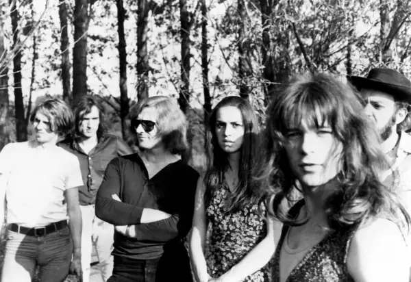 Un groupe rock allemand des années 70, avec des membres aux cheveux longs et des tenues décontractées, posant devant des arbres.