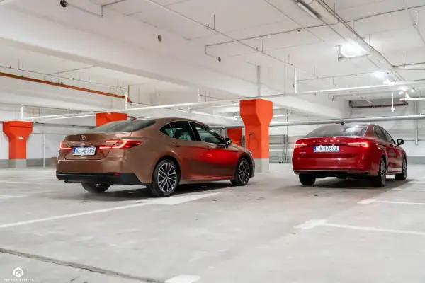 Brązowa Toyota Camry i czerwona Skoda Superb stoją w garażu podziemnym.