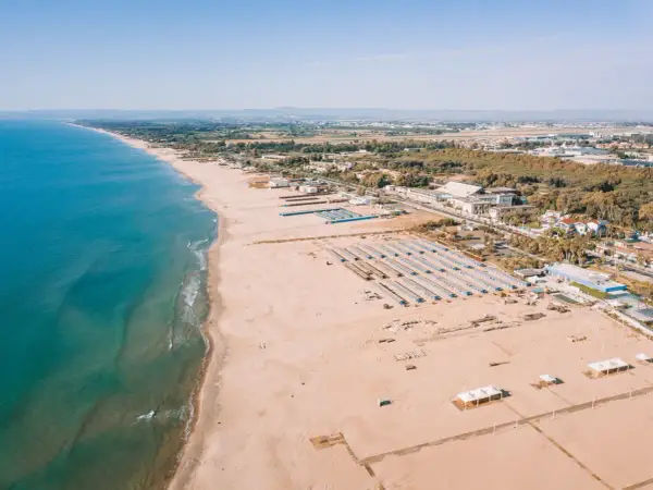Vue aérienne d'une longue plage de sable fin bordée par la mer bleue, avec des rangées de parasols et des bâtiments à Catane, Sicile.