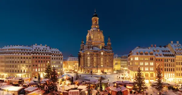Śnieżny jarmark w Dreźnie. W tle Frauenkirche, po bokach oświetlone kamienice i choinki.
