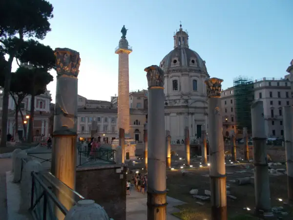 Antiche colonne onorarie illuminate di sera, con una cupola sullo sfondo.