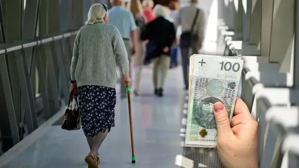 Emerytka z laską idzie korytarzem, obok stos banknotów 100 zł. Waloryzacja emerytur 2026 - tabela.