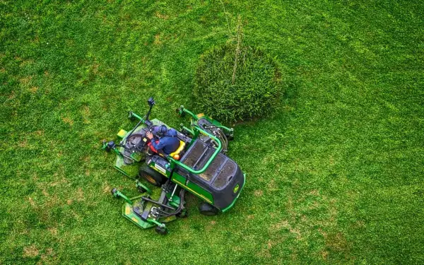 Un homme est assis sur un tracteur tondeuse, prêt à passer la tondeuse le dimanche. L'herbe est d'un vert éclatant.