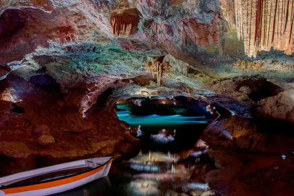 Interior de cueva con estalactitas, agua turquesa y una barca. Consulta las cuevas de Vall d'Uixó horarios y precios para tu visita.