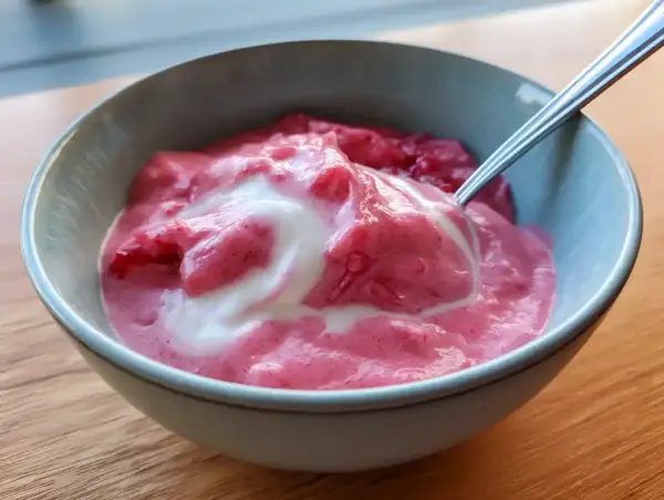 En skål med krämig rabarbercurd med en virvel av grädde. Perfekt för en somrig fika.