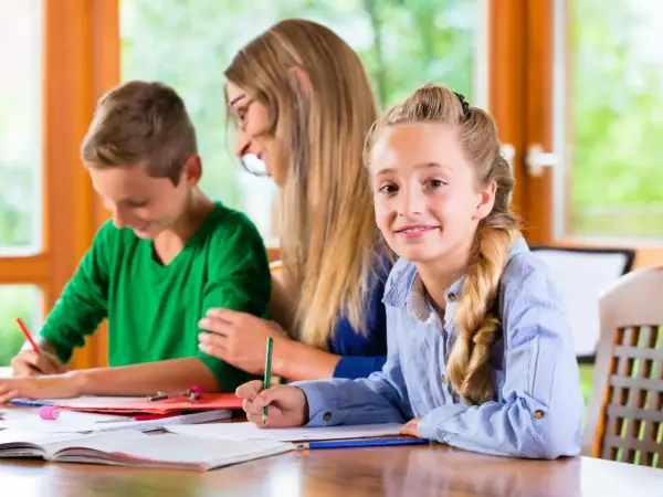 Dziewczynka uśmiecha się, pisząc lekcje. Obok niej brat i mama, co to za nauka!