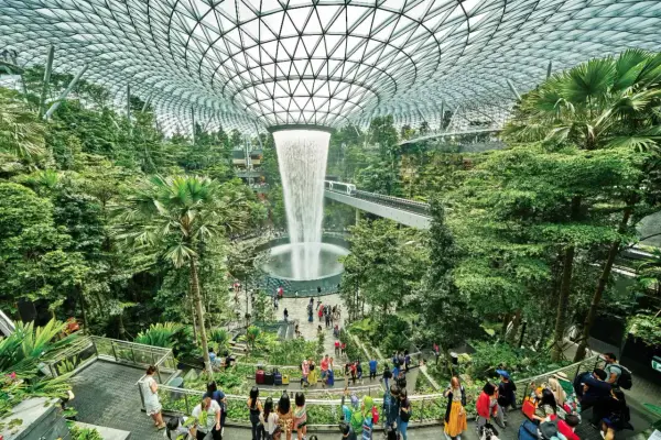 Imponerande vattenfall och frodig grönska under glastaket på singapore flygplats. Människor njuter av den unika miljön.