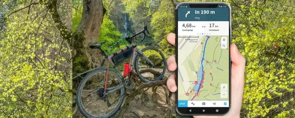 Rower gravelowy przy wodospadzie, a obok smartfon z aplikacją komoot pokazującą trasę i dystans.