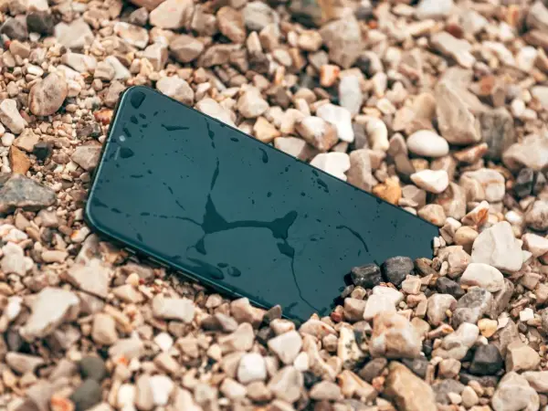 Smartfon leży na kamieniach, mokry, ale wytrzymały zgodnie ze **standardem militarnym MIL-STD-810H**.