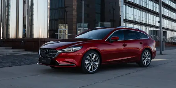 Czerwona Mazda 6 kombi na tle nowoczesnego budynku. Poznaj jej imponujące mazda 6 wymiary i styl.