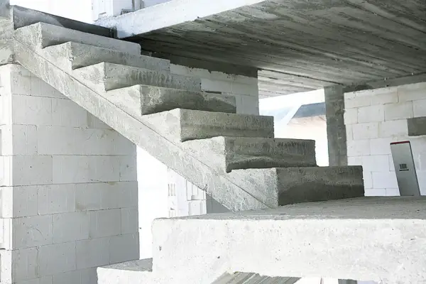 Surowe, betonowe schody czekają na wykończenie. W tle białe bloczki budowlane.