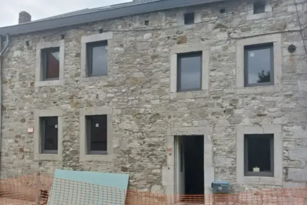 Façade d'une maison en pierre, en cours d'isolation. Fenêtres neuves et entrée ouverte sur un chantier.