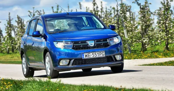 Niebieska Dacia Sandero 2025 jedzie przez kwitnący sad.