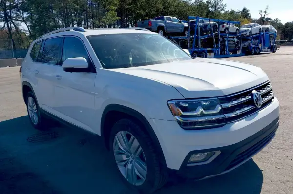 Biały VW Atlas stoi na parkingu, w tle widać lawetę z innymi samochodami.