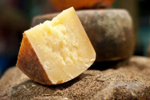 Un pezzo di formaggio sardo stagionato, con crosta scura e pasta gialla, riposa su un letto di spezie macinate.