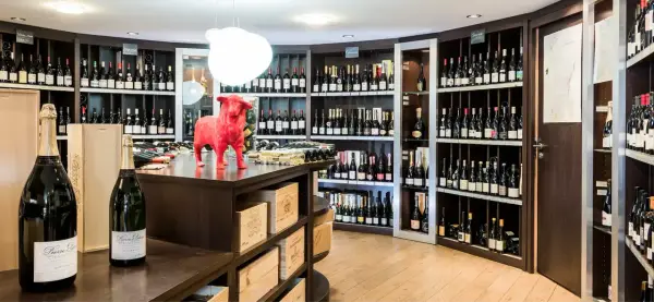 Cave à vin avec étagères remplies de bouteilles, une statue de taureau rouge et des bouteilles de champagne au premier plan.