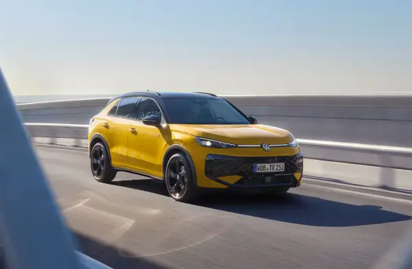 Żółty Volkswagen Cross pędzi po drodze, błyszcząc w słońcu.