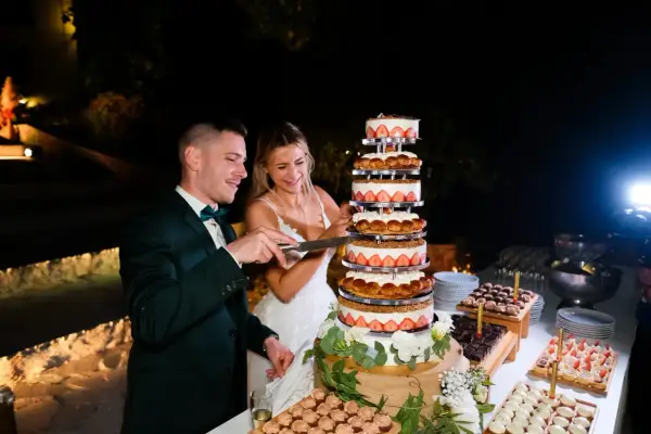 Un couple coupe un dessert mariage original, une tour de gâteaux aux fraises et à la crème, lors d'une réception nocturne.