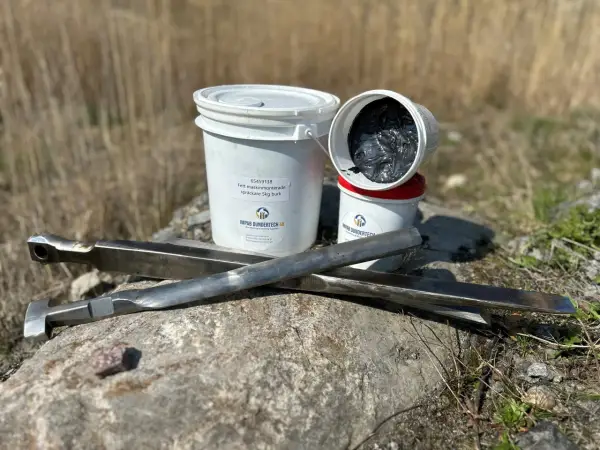 Fett till dragkrok och verktyg ligger på en sten. Två burkar med fett, varav en öppen, syns bredvid.