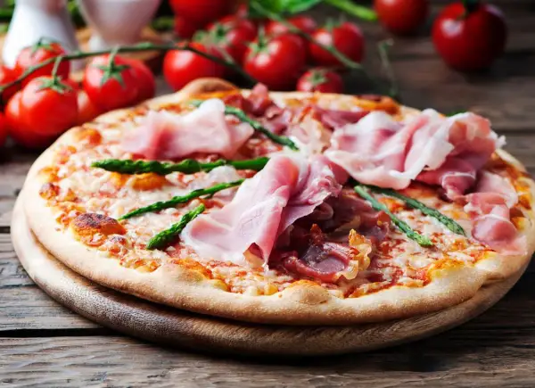 Pyszna pizza ze szparagami i szynką parmeńską, ozdobiona świeżymi pomidorkami koktajlowymi.