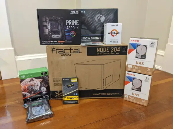 Composants pour installer un NAS : carte mère ASUS, processeur AMD Athlon, boîtier Fractal Design, alimentation, RAM Corsair, et deux disques durs Toshiba 8 To.