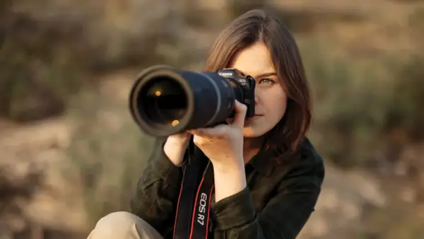 Kobieta z aparatem Canon EOS R7, skupiona na kadrze. Dopasowuje ustawienia aparatu, by uchwycić idealny moment.