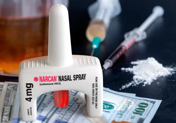 Nasalny spray nalokson, strzykawki z substancją, biały proszek i banknoty dolarowe.