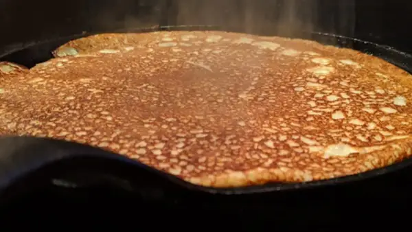 En gyllene, nygräddad pannkaka steker i en gjutjärnspanna. Perfekt för en glutenfri frukost eller fika.