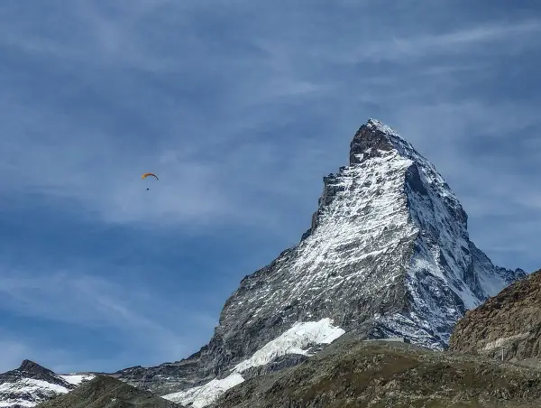 Majestatyczny polski Matterhorn, pokryty śniegiem, góruje nad krajobrazem. Na błękitnym niebie, wśród chmur, szybujący paralotniarz.