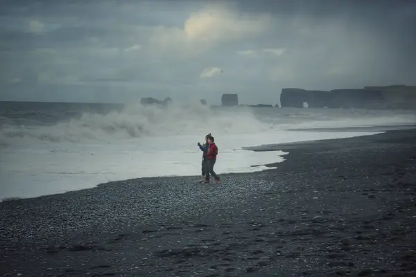 Para spaceruje po czarnej plaży Islandii, podczas gdy fale rozbijają się o brzeg.