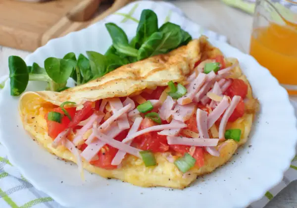 Pyszny omlet bez mąki z szynką, pomidorami i szczypiorkiem, podany z sałatką. Idealny na szybkie śniadanie.
