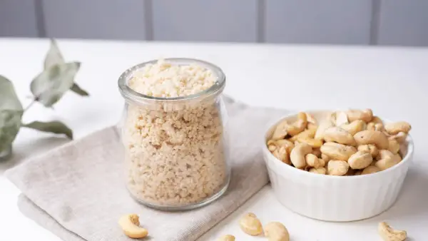 Zutaten für veganen Parmesan selber machen: Cashewkerne in einer Schüssel und fertig gemahlene Masse in einem Glas.