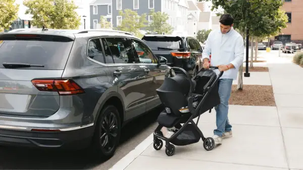 Hombre empuja un cochecito con un sistema sujeción infantil silla coche, junto a un coche gris.
