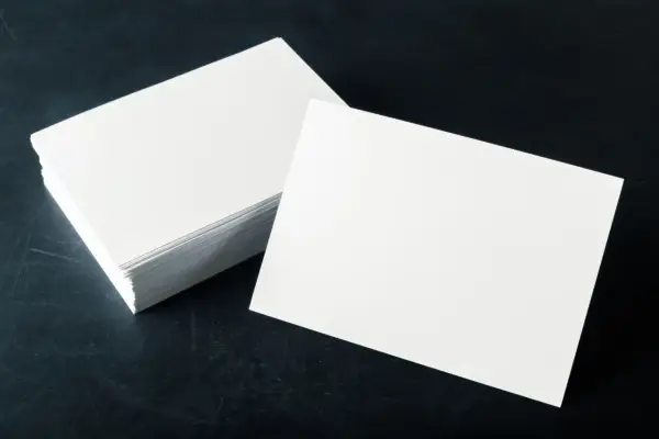Pila de tarjetas blancas sobre fondo oscuro. El gramaje del papel es ideal para impresiones de alta calidad.