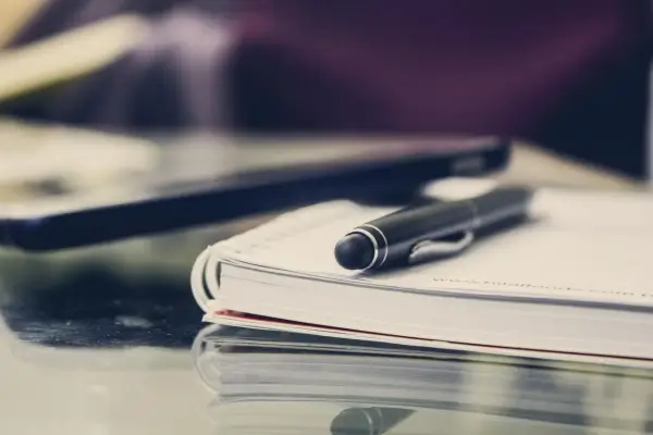 Czarny długopis spoczywa na otwartym notatniku. Obok leży laptop, gotowy do pracy. FGŚP.