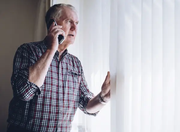 Zaniepokojony starszy mężczyzna rozmawia przez telefon, szukając informacji, gdzie zgłosić zaniedbywanie osoby starszej.