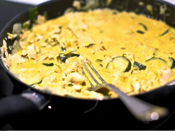 Pyszne curry z cukinią i kurczakiem w kremowym sosie, gotowe do podania. Widelec czeka na pierwszy kęs.