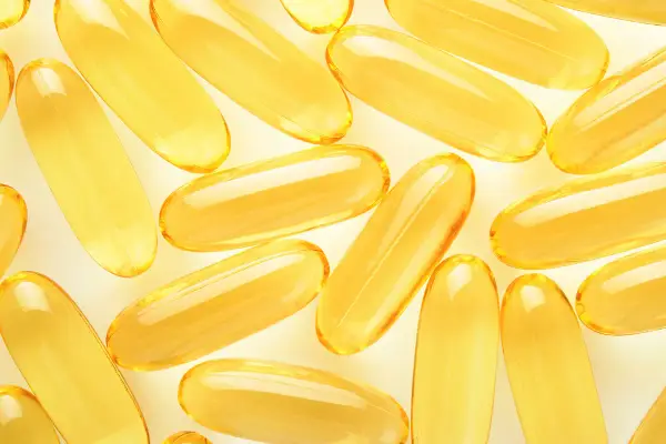 Żółte kapsułki omega 3 ułożone na jasnym tle. Kiedy brać omega 3? Najlepiej po posiłku, by zwiększyć wchłanianie.
