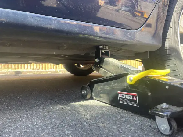 Lewarek podłożony pod wzmocnienie progu samochodu. Widać podnośnik i miejsce, gdzie podłożyć lewarek, by bezpiecznie podnieść auto.