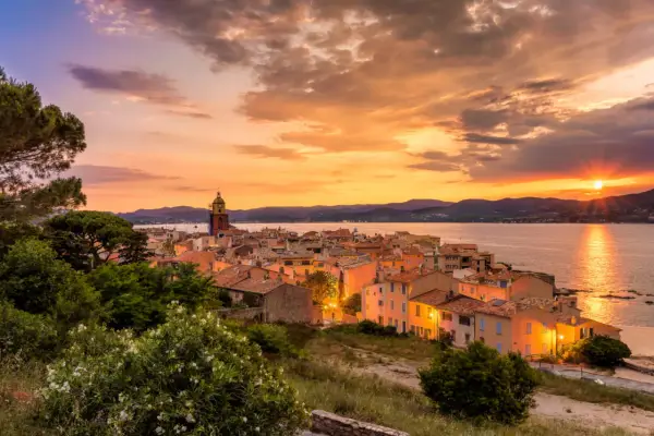 Sonnenuntergang über St. Tropez. Die Sonne versinkt im Meer, beleuchtet die Stadt und den Kirchturm in warmen Farben.