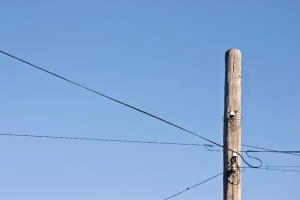 Drewniany słup z izolatorami, na którym widać światłowód na słupach. Linie energetyczne przecinają błękitne niebo.