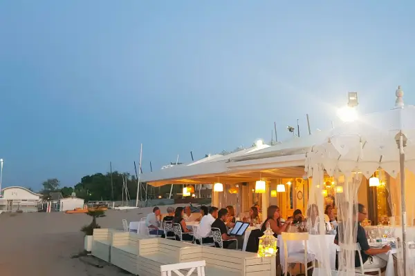 Serata in uno dei ristoranti della Riviera Romagnola, con tavoli apparecchiati sulla sabbia e luci soffuse.