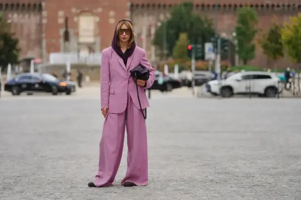 Kobieta w garniturze w kolorze mauve, z szerokimi nogawkami spodni, pozuje na tle miasta.