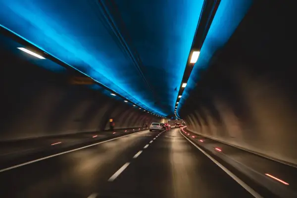 Jadące samochody w tunelu drogowym z niebieskim oświetleniem sufitowym.
