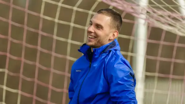 Uśmiechnięty piłkarz w niebieskiej kurtce, gotowy do gry w stylu tiki-taka.