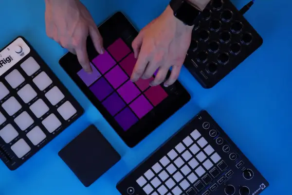 Des mains jouent sur une tablette avec des pads colorés, entourée de contrôleurs pour créer de la musique. Un sampler sans ordinateur en action.