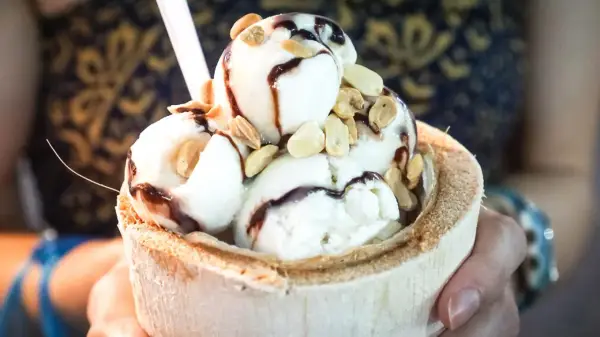 Cremiges Pina Colada Eis in einer Kokosnussschale, beträufelt mit Schokoladensauce und garniert mit Nüssen. Ein tropischer Genuss!