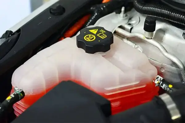 Depósito de refrigerante de coche con líquido rojo. La tapa negra tiene símbolos de advertencia. Se puede echar agua normal al coche si es necesario.