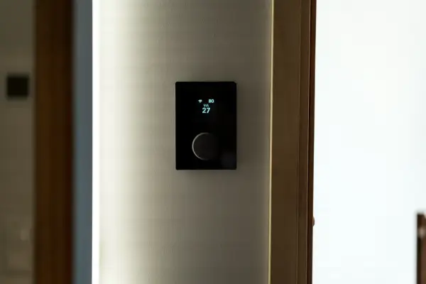 Nowoczesny termostat steruje ogrzewaniem elektrycznym, pokazując temperaturę 27 stopni.