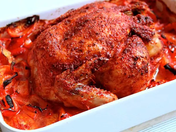 Helstekt tandoori kyckling med rostade tomater och paprika i en vit ugnsform. Kryddig och saftig.